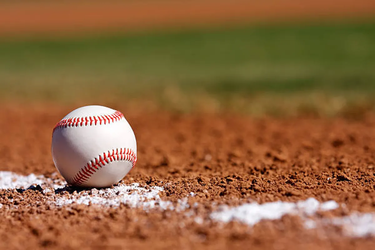 A close-up of a baseball resting on a dirt infield, with crisp white chalk lines clearly visible, evoking the classic feel of a ballpark. The scene hints at game moments, youth tournaments, and the excitement of local sporting events.