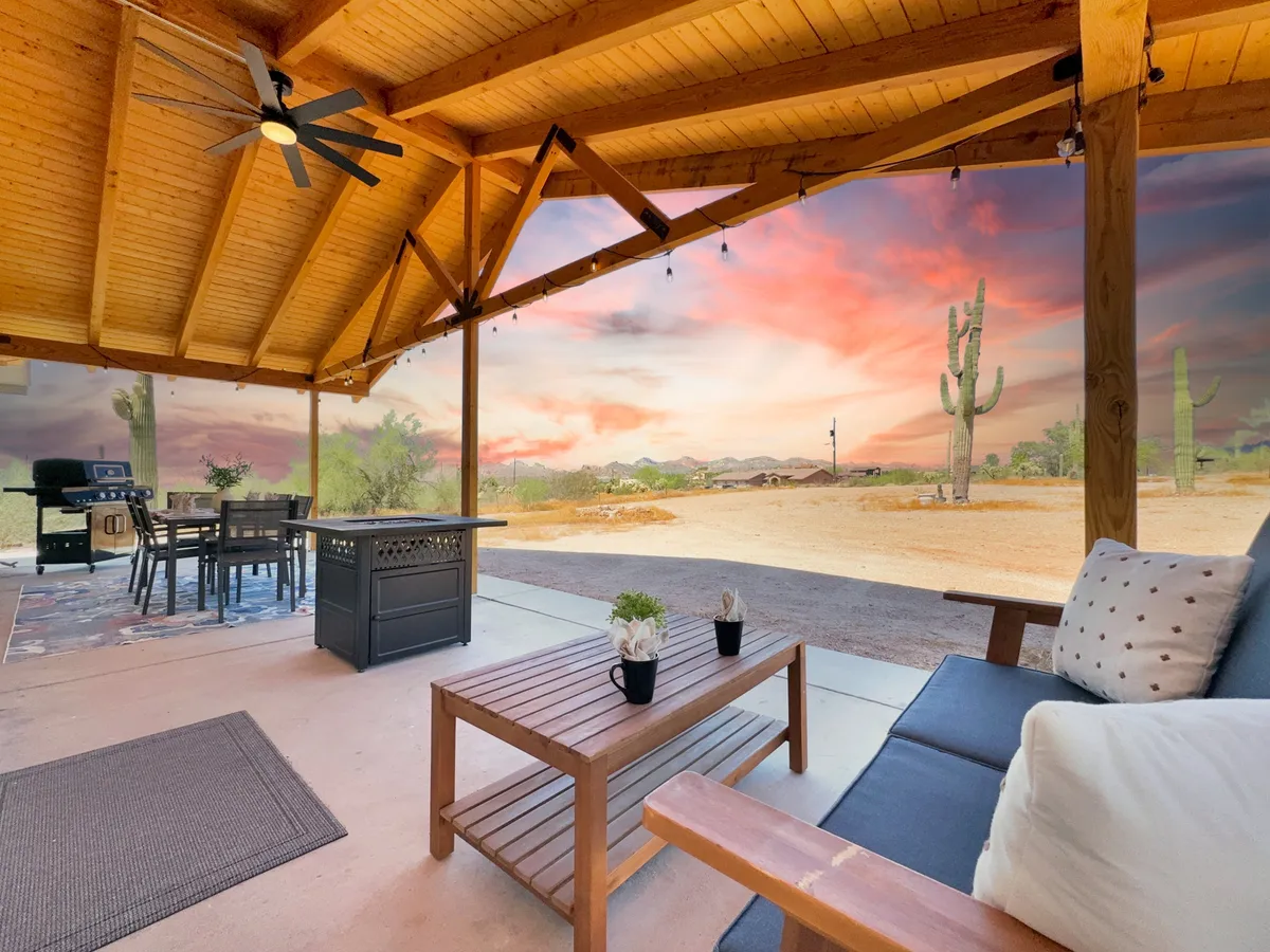 A serene outdoor dining and lounge space, complete with a wooden ceiling, dining table, sunset sky, and cacti beyond. The mood is relaxed and tranquil, perfect for stargazing, barbecues, or winding down after a full day of entertainment.