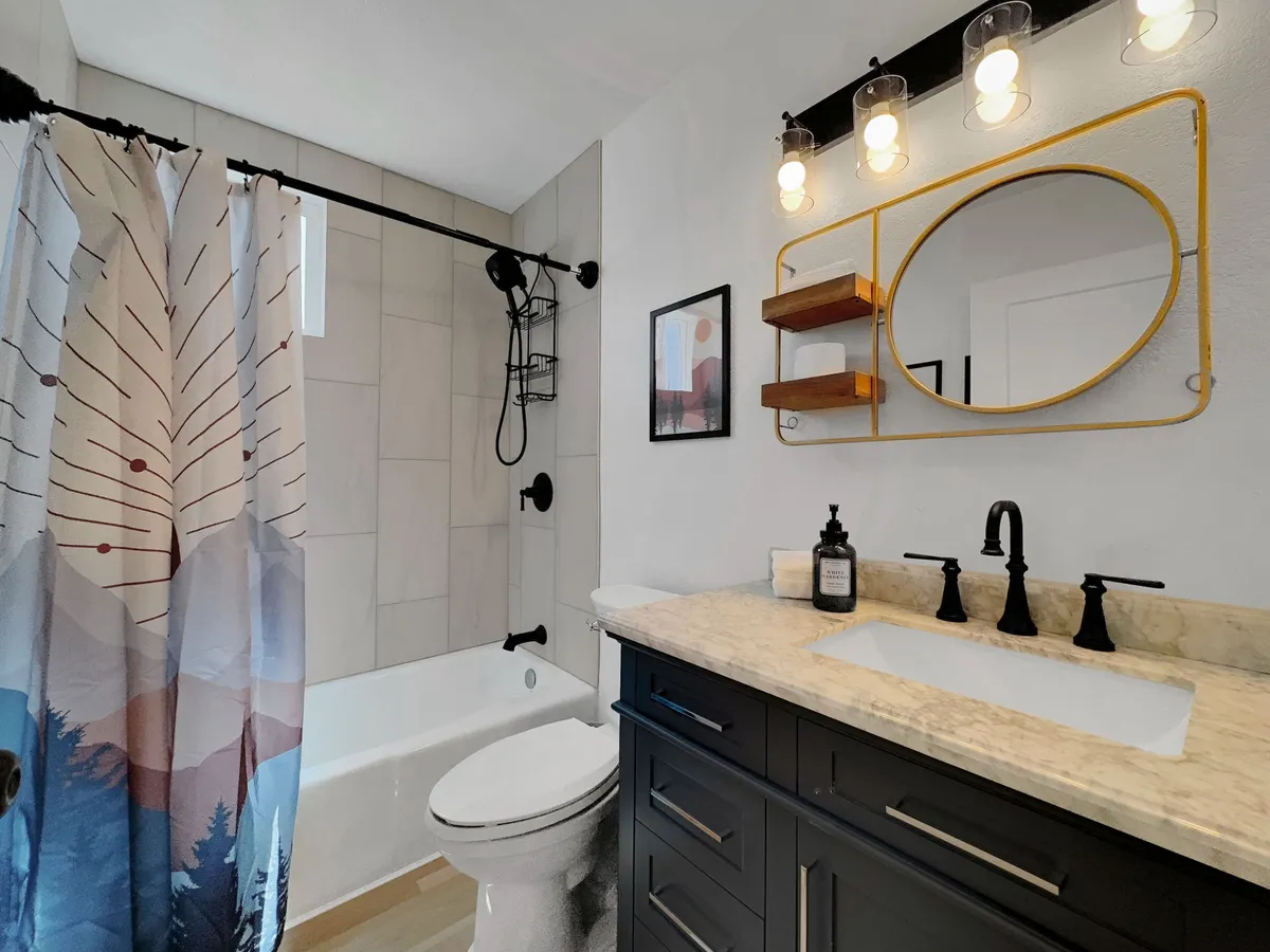 A stylish, modern bathroom with an artistic shower curtain, a sleek vanity and sink, and a decorative mirror with shelves. The inviting ambiance and practical layout make it conducive to both privacy and comfort.