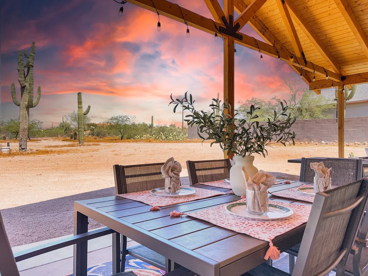 An outdoor dining area is set against tall cacti and a vibrant sunset sky. The table is elegantly set, suggesting opportunities for intimate meals or evening socializing while surrounded by nature.