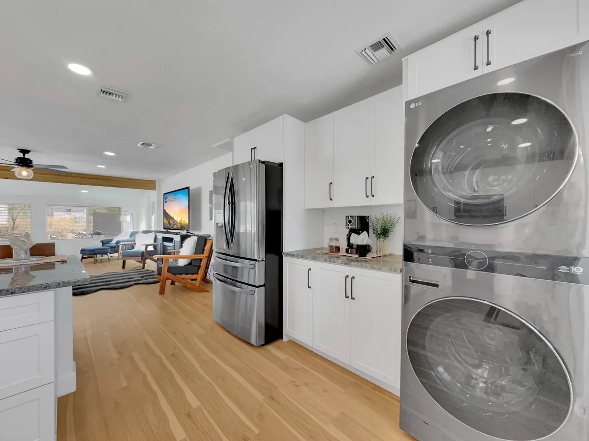 A modern open interior featuring a stainless steel refrigerator, stacked washer and dryer, granite countertops, and bright white cabinetry—all in a connected layout that hints at easy access to both the kitchen and laundry area.