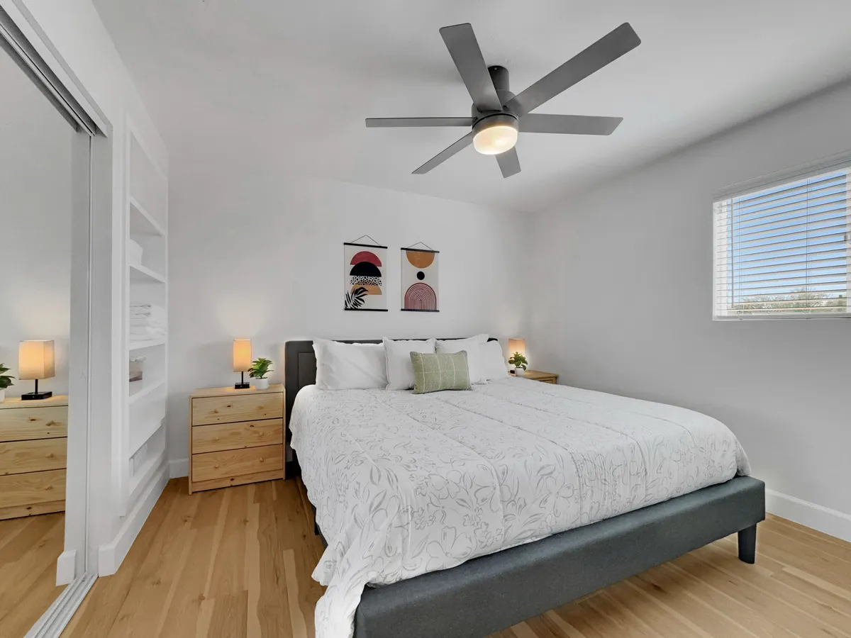 A serene bedroom featuring a king-sized bed with crisp white linens, coordinating wall art, and matching nightstands with lamps. Soft natural light filters into the space, creating an atmosphere of relaxation and comfort.